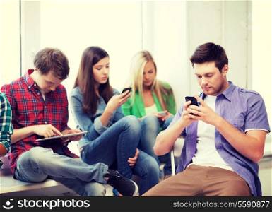 education and internet concept - students looking into phones and tablet pc