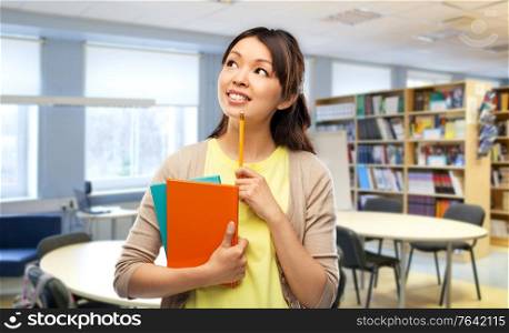 education and knowledge concept - asian student woman with books and pencil over school library background. asian student woman with books at library