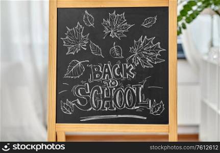 education and learning concept - autumn leaves and back to school words drawn with chalk on chalkboard at home. back to school lettering drawn on chalkboard