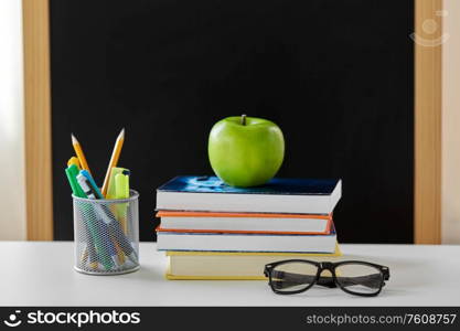 education and learning concept - books, apple, chalkboard and school supplies on table at home. books, apple and school supplies on table at home