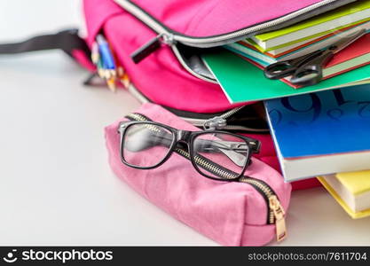 education and learning concept - close up of pink backpack with books and school supplies, green apple on table at home. backpack, apple and school supplies on table