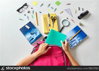 education and learning concept - hands packing pink backpack with books and school supplies on table. hands with backpack, books and school supplies