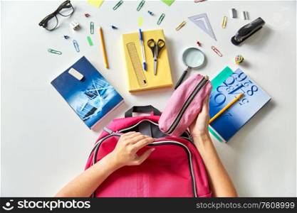 education and learning concept - hands packing pink backpack with pencil-case, books and school supplies on table. hands with backpack, books and school supplies