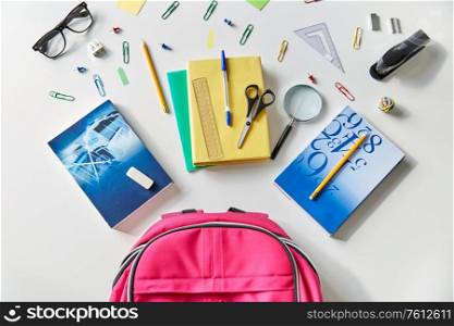 education and learning concept - pink backpack with books and school supplies on table. pink backpack with books and school supplies