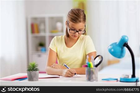 education and learning concept - student girl writing to notebook at home. student girl writing to notebook at home