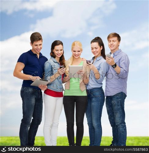 education and modern technology concept - smiling students using smartphones and tablet pc