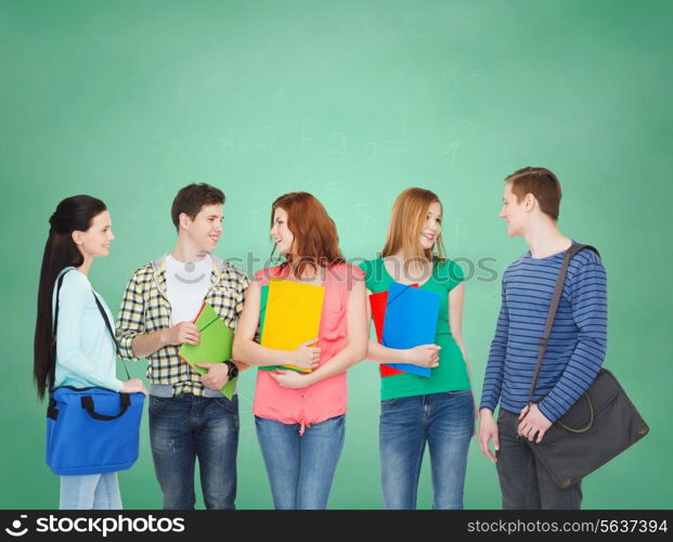 education and people concept - group of smiling students with bags and folders having discussion