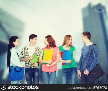 education and people concept - group of smiling students with bags and folders having discussion