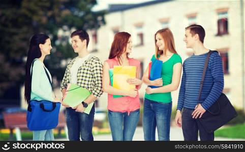 education and people concept - group of smiling students with bags and folders having discussion