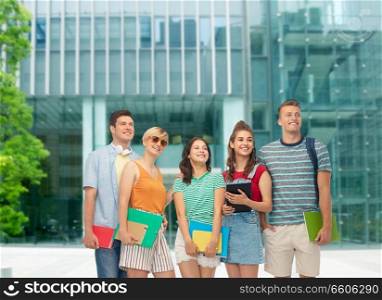 education and people concept - group of smiling students with notebooks, books and folders over modern school or university building background. students with books and folders over modern school