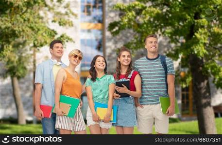 education and people concept - group of smiling students with notebooks, books and folders over campus background. students with books and folders over campus