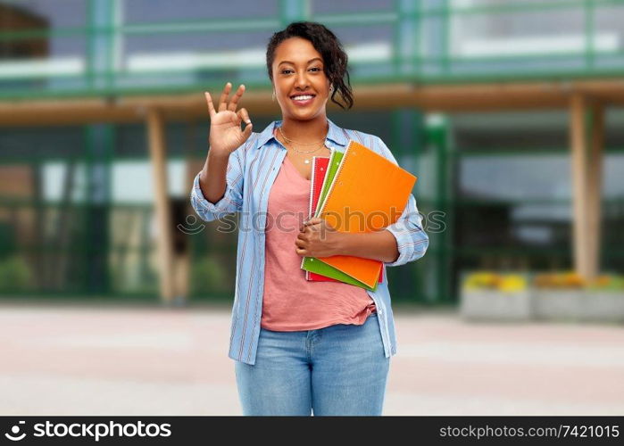 education and people concept - happy african american young student woman with notebooks over school yard background. african american student woman with notebooks