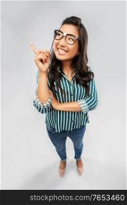 education and people concept - happy smiling asian young student woman in broken glasses pointing finger up over grey background. smiling asian student woman pointing finger up