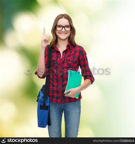 education and people concept - smiling female student in eyeglasses with bag and notebooks showing finger up over green background