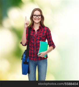 education and people concept - smiling female student in eyeglasses with bag and notebooks showing finger up over green background