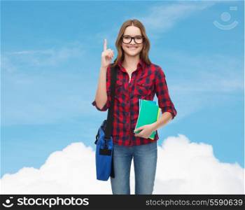 education and people concept - smiling female student in eyeglasses with bag and notebooks showing finger up over blue sky background