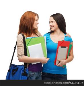 education and people concept - two smiling students with bag and folders standing looking at each other