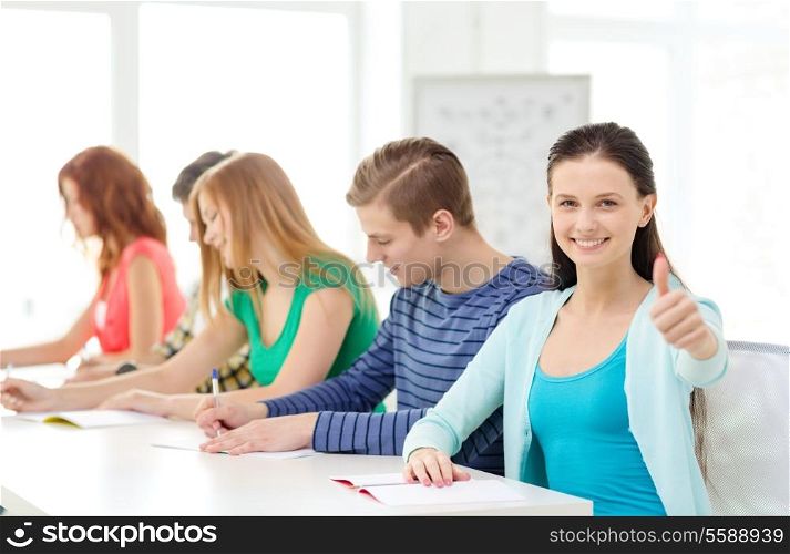 education and school concept - five smiling students with textbooks and girl in front showing thumbs up at school