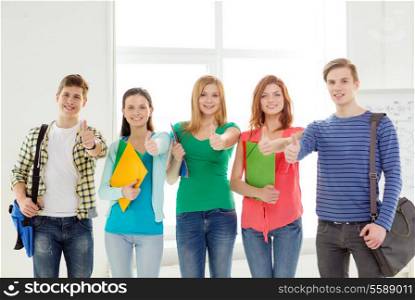 education and school concept - group of smiling students with bags and folders at school showing thumbs up