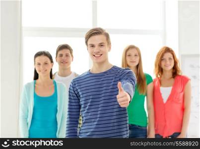 education and school concept - group of smiling students with teenage boy in front showing thumbs up
