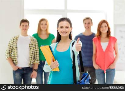 education and school concept - group of smiling students with teenage girl in front with bag and folders showing thumbs up
