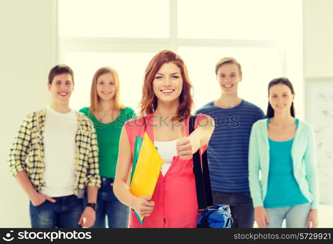 education and school concept - group of smiling students with teenage girl in front with bag and folders showing thumbs up