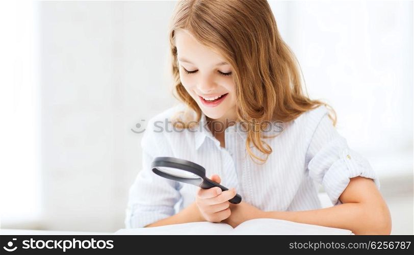 education and school concept - little student girl reading book with magnifier at school. girl reading book with magnifier at school