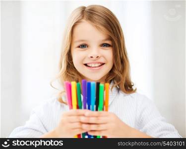 education and school concept - little student girl showing colorful felt-tip pens at school