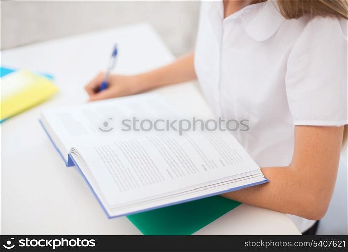 education and school concept - little student girl with book writing in notebook at school