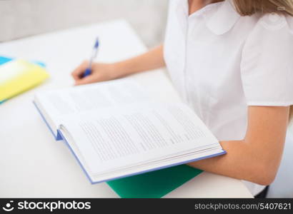 education and school concept - little student girl with book writing in notebook at school