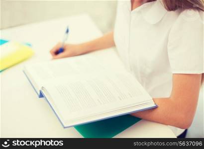 education and school concept - little student girl with book writing in notebook at school
