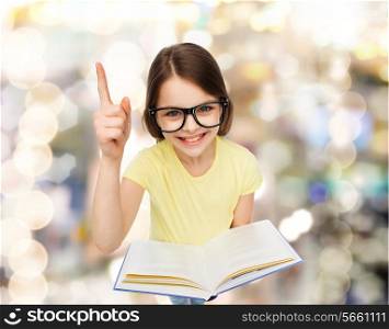 education and school concept - smiling little student girl in eyeglasses with book and finger up