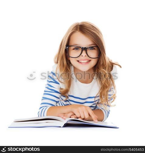 education and school concept - smiling little student girl with book and eyeglasses lying on the floor