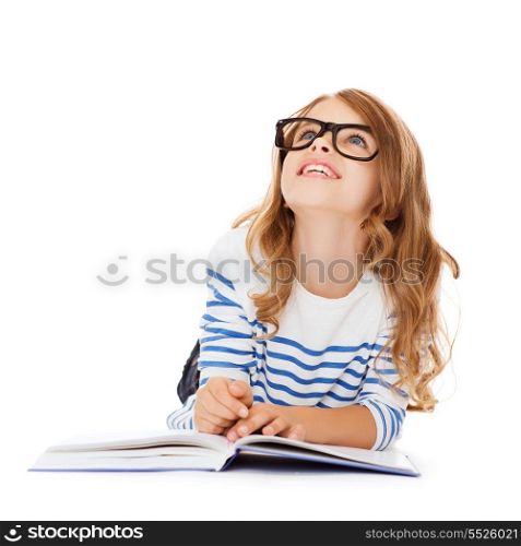 education and school concept - smiling little student girl with book and eyeglasses lying on the floor and looking up