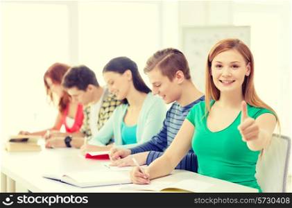education and school concept - smiling students with textbooks and books and girl in front showing thumbs up at school