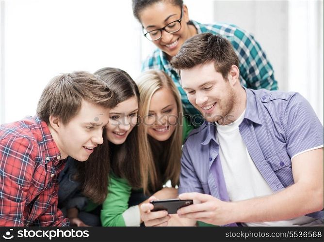 education and technology concept - group of students looking at smartphone at school