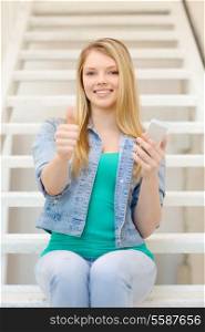 education and technology concept - smiling female student with smartphone sitting on staircase and showing thumbs up
