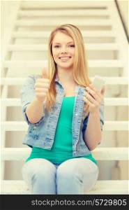 education and technology concept - smiling female student with smartphone sitting on staircase and showing thumbs up