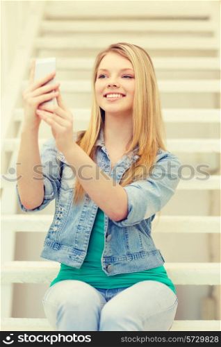 education and technology concept - smiling female student with smartphone sitting on staircase and taking picture