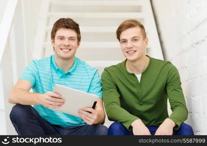 education and technology concept - smiling male students with tablet pc computer sitting on staircase