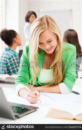 education and technology concept - smiling student girl writing in notebook at school