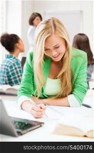 education and technology concept - smiling student girl writing in notebook at school