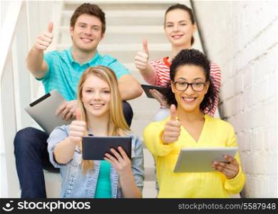 education and technology concept - smiling students with tablet pc computer sitting on staircase and showing thumbs up