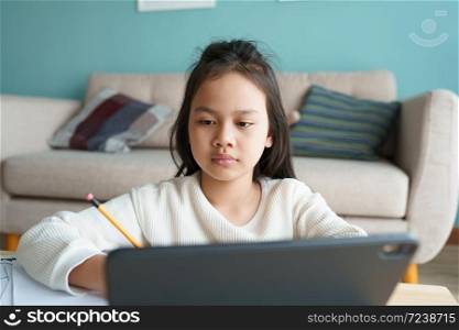 Education. Asian girl is learning with online tutor via the internet on tablet digital at home morning. Asia children watch computer and write homework. Concept of online learning at home