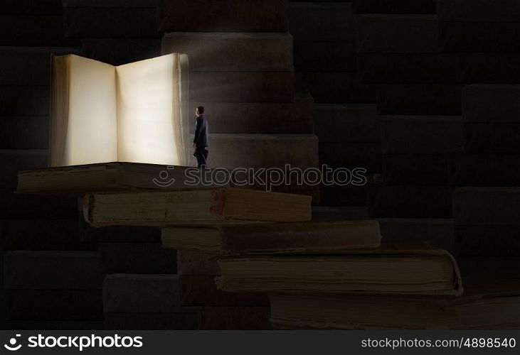Education benefit. Big old opened book and miniature of businessman