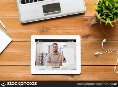 education, blogging and technology concept - close up of tablet pc computer, laptop and earphones on wooden table with male teacher or blogger on screen. tablet pc with male teacher or blogger on screen