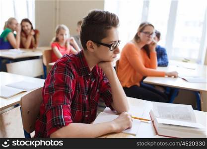 education, bullying and people concept - student boy in glasses reading book and group of classmates at school lesson