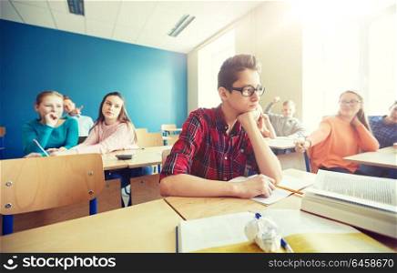 education, bullying, conflict, social relations and people concept - student boy in glasses reading book and suffering of classmates mockery at school. classmates laughing at student boy in school