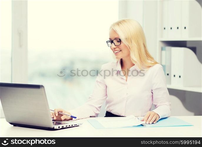education, business and technology concept - smiling businesswoman or student in eyeglasses with laptop computer and documents in office