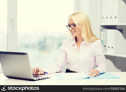 education, business and technology concept - smiling businesswoman or student in eyeglasses with laptop computer and documents in office